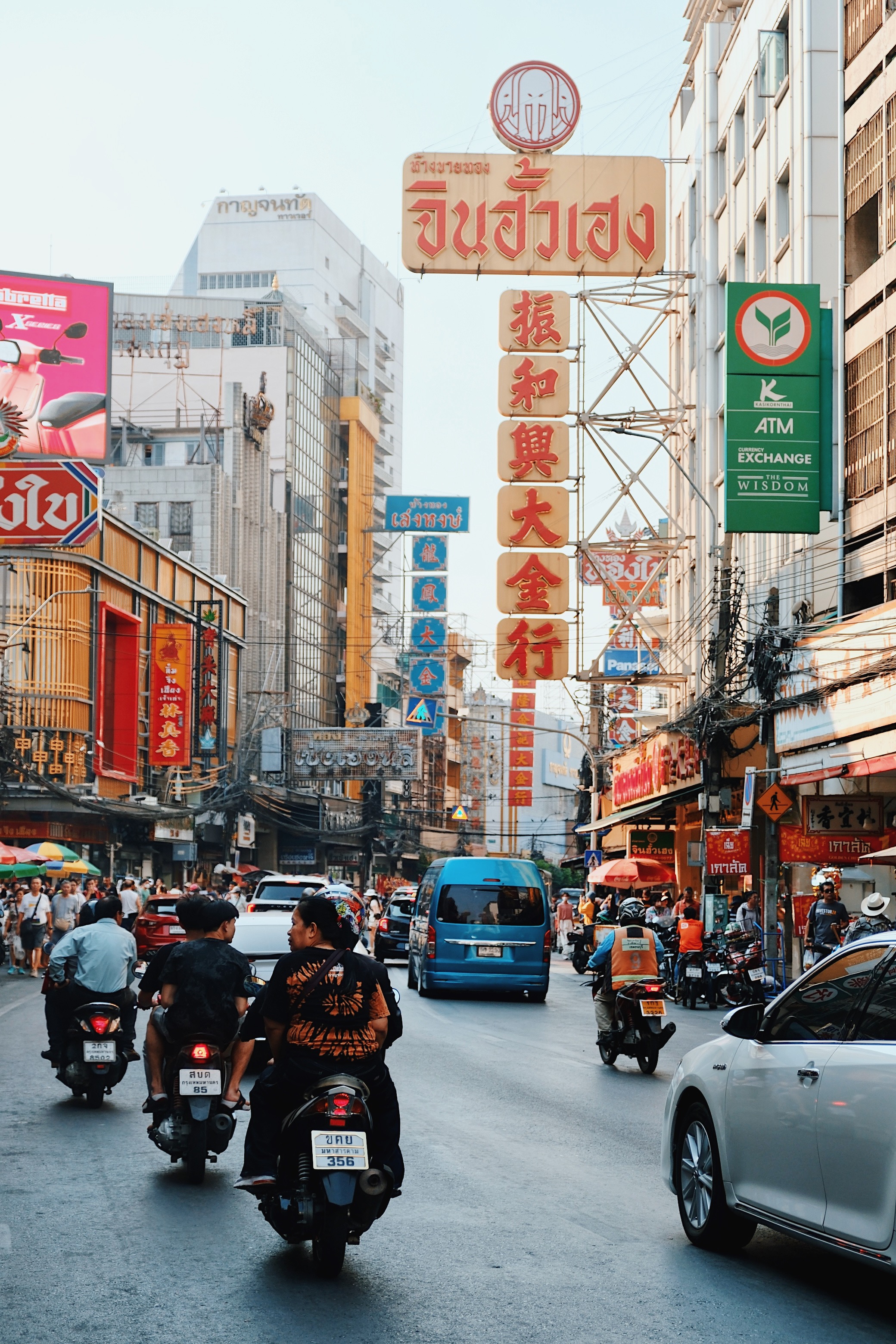 A chaotic street scene in Bangkok’s Chinatown, where motorbikes and cars navigate through a dense maze of red and gold Chinese signage.