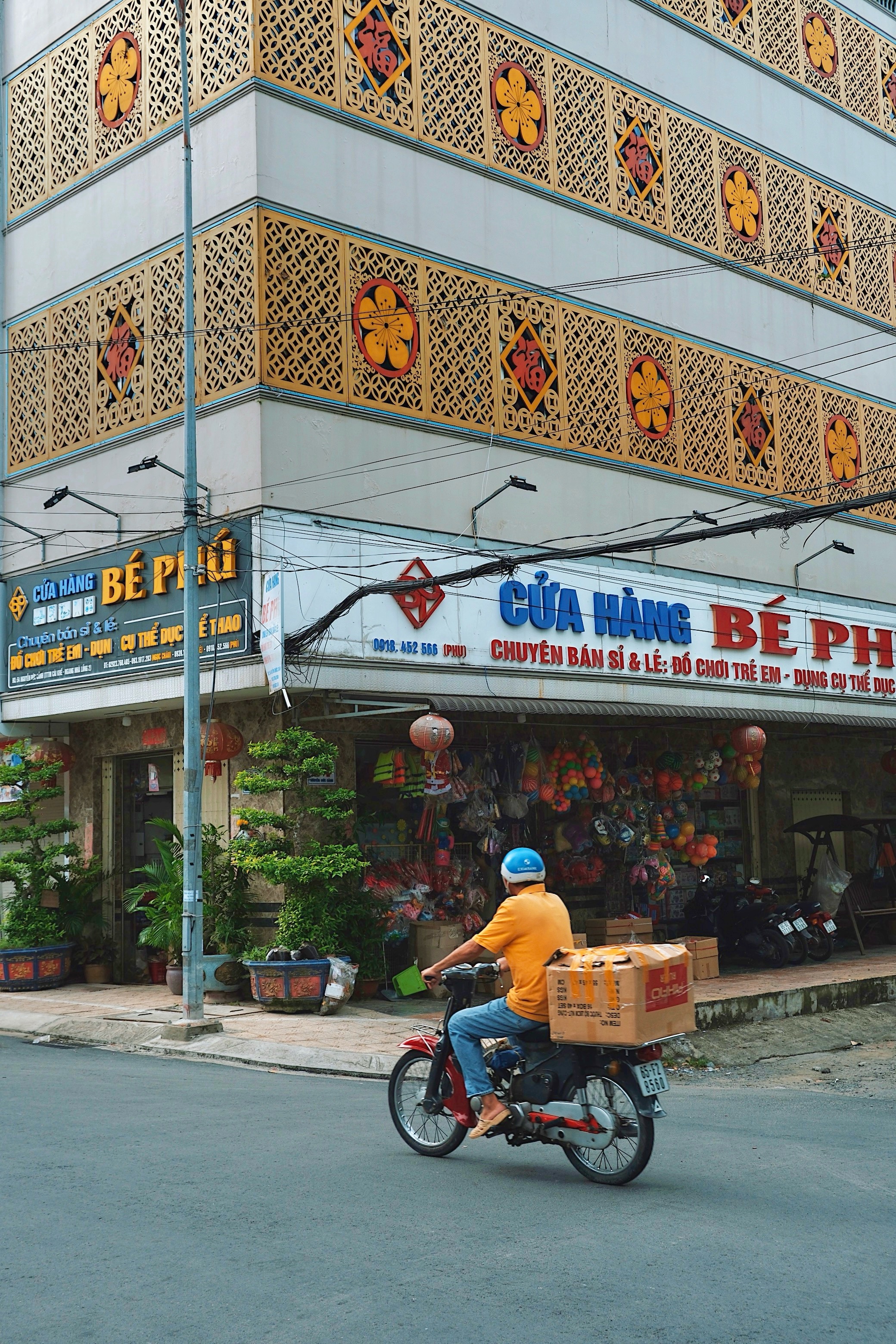 A man rides a motorbike past a highly decorated modernist-style building in Cần Thơ, showcasing a fusion of traditional and contemporary Vietnamese architectural influences.
