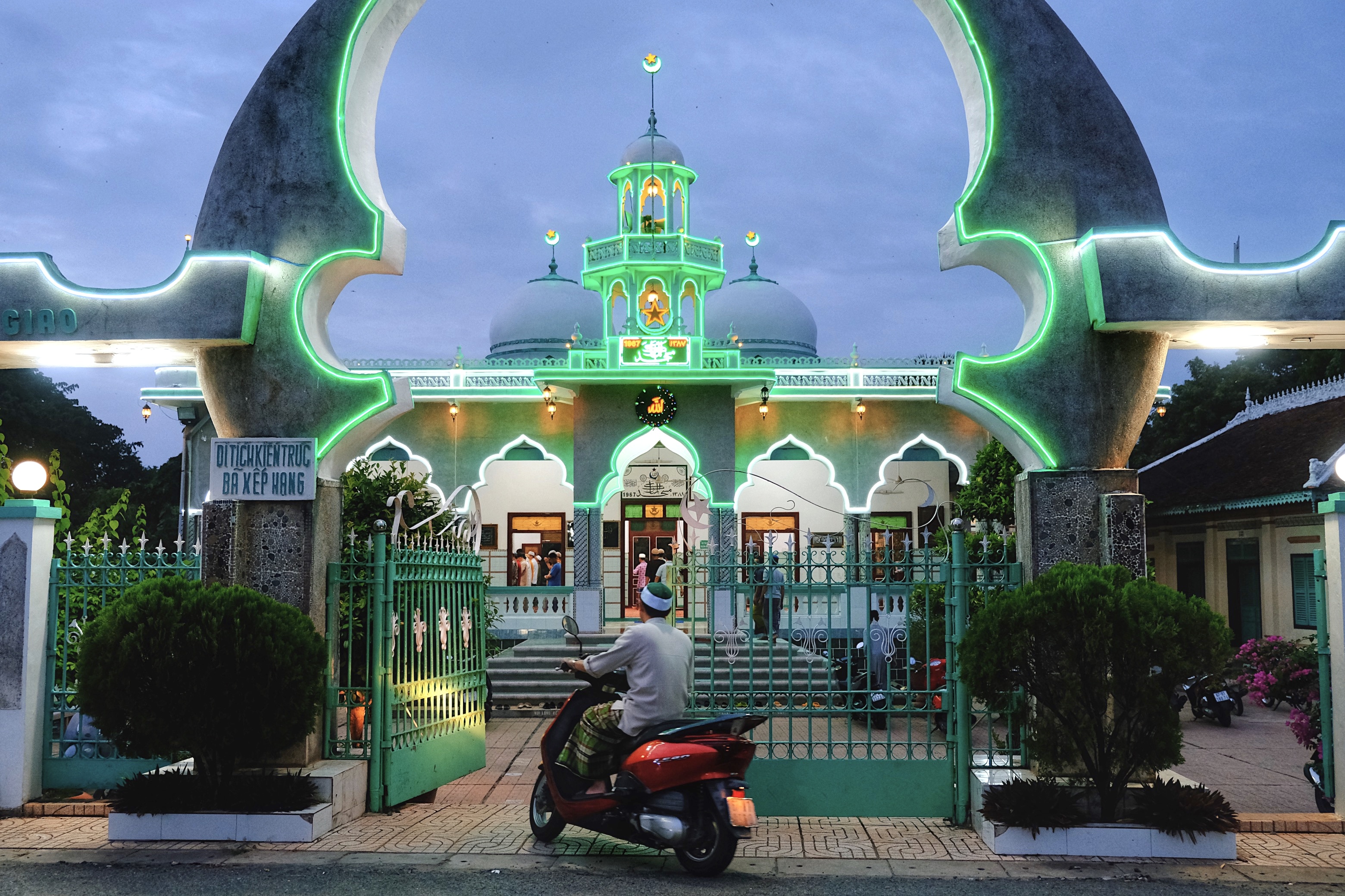Neon-lit mosque in Châu Đốc, Vietnam, blending Islamic architectural motifs with local modernist concrete forms, illuminated by green fluorescent outlines at dusk