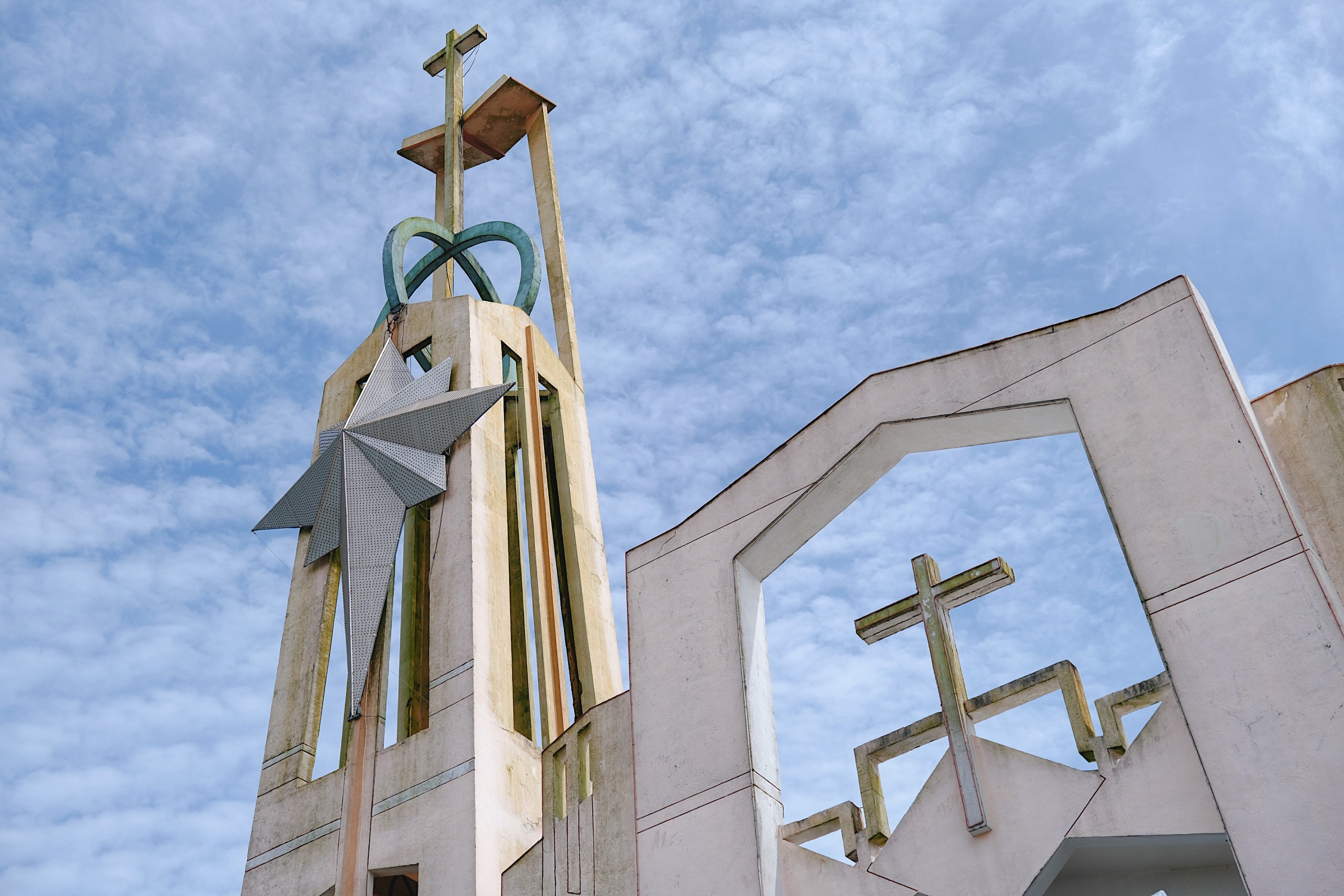 A towering Vietnamese church steeple with an avant-garde modernist design, featuring crosses, geometric elements, and a cloudy sky
