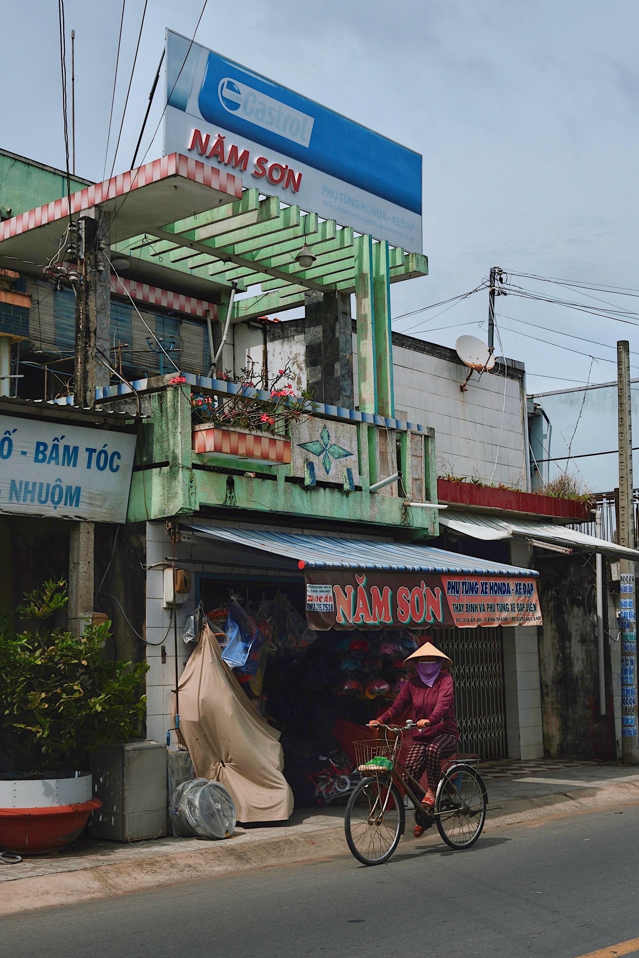Everyday life in Ben Tre, Vietnam: A cyclist rides past a green modernist building featuring geometric concrete louvers.
