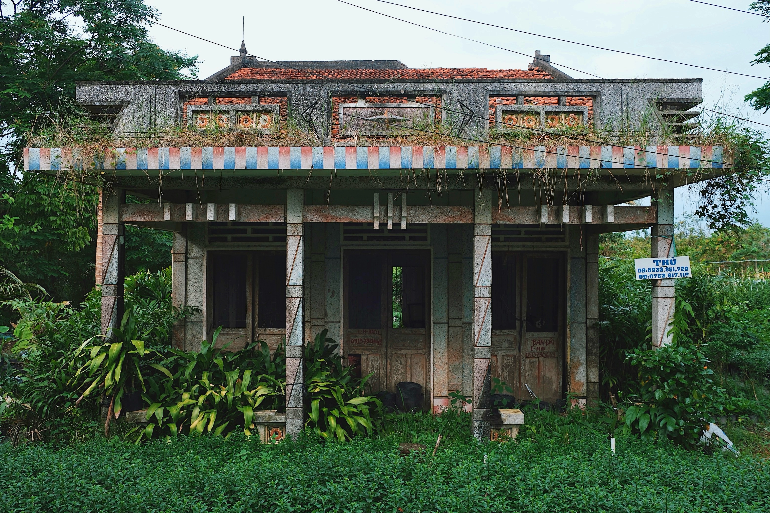 A countryside modernist house in Ben Tre with red and blue tiled columns, geometric facades, and a blend of modernist and local architectural styles.