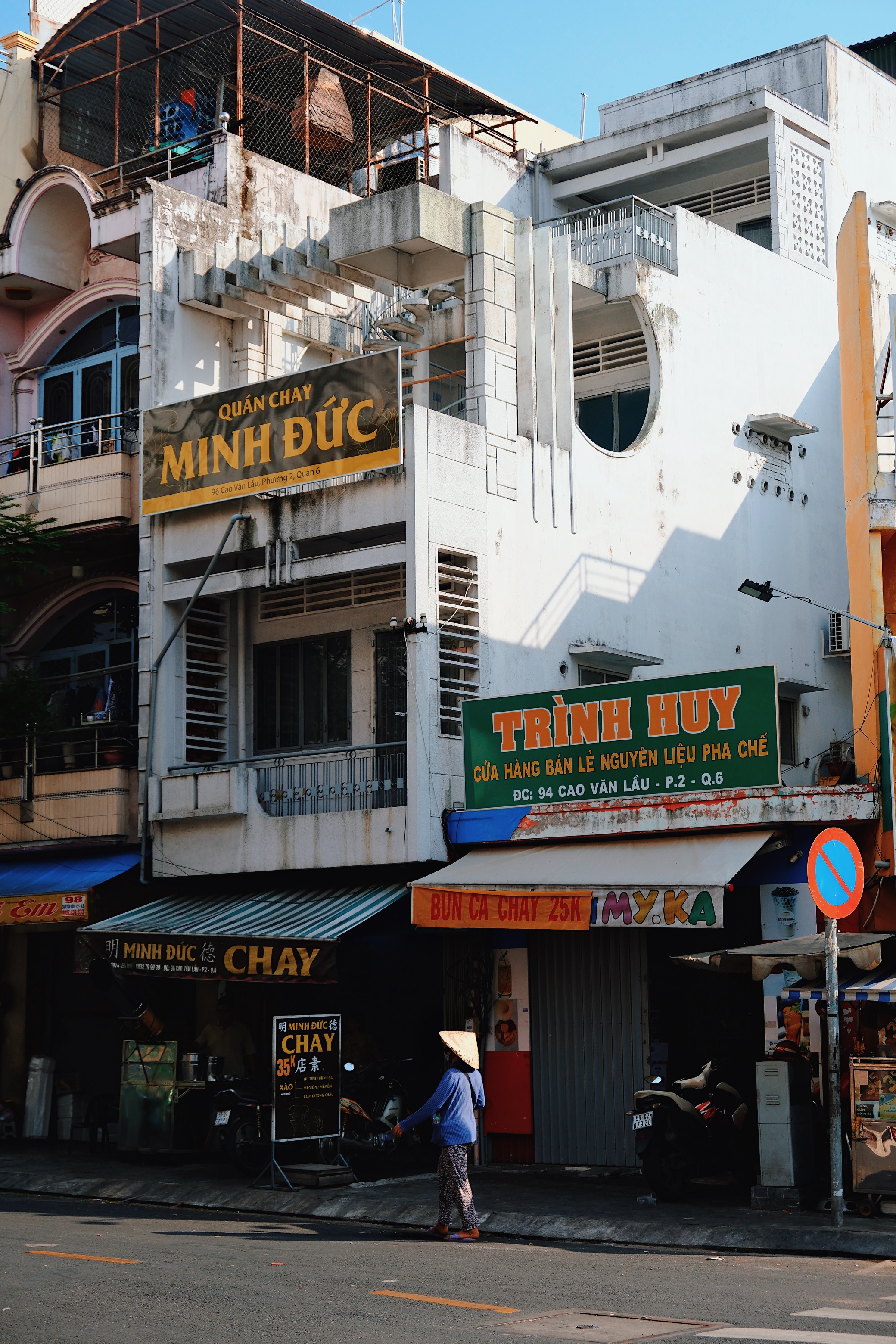A Vietnamese pedestrian in a conical hat walks past a modernist building in Ho Chi Minh City, showcasing the contrast between daily life and mid-century modern architecture.