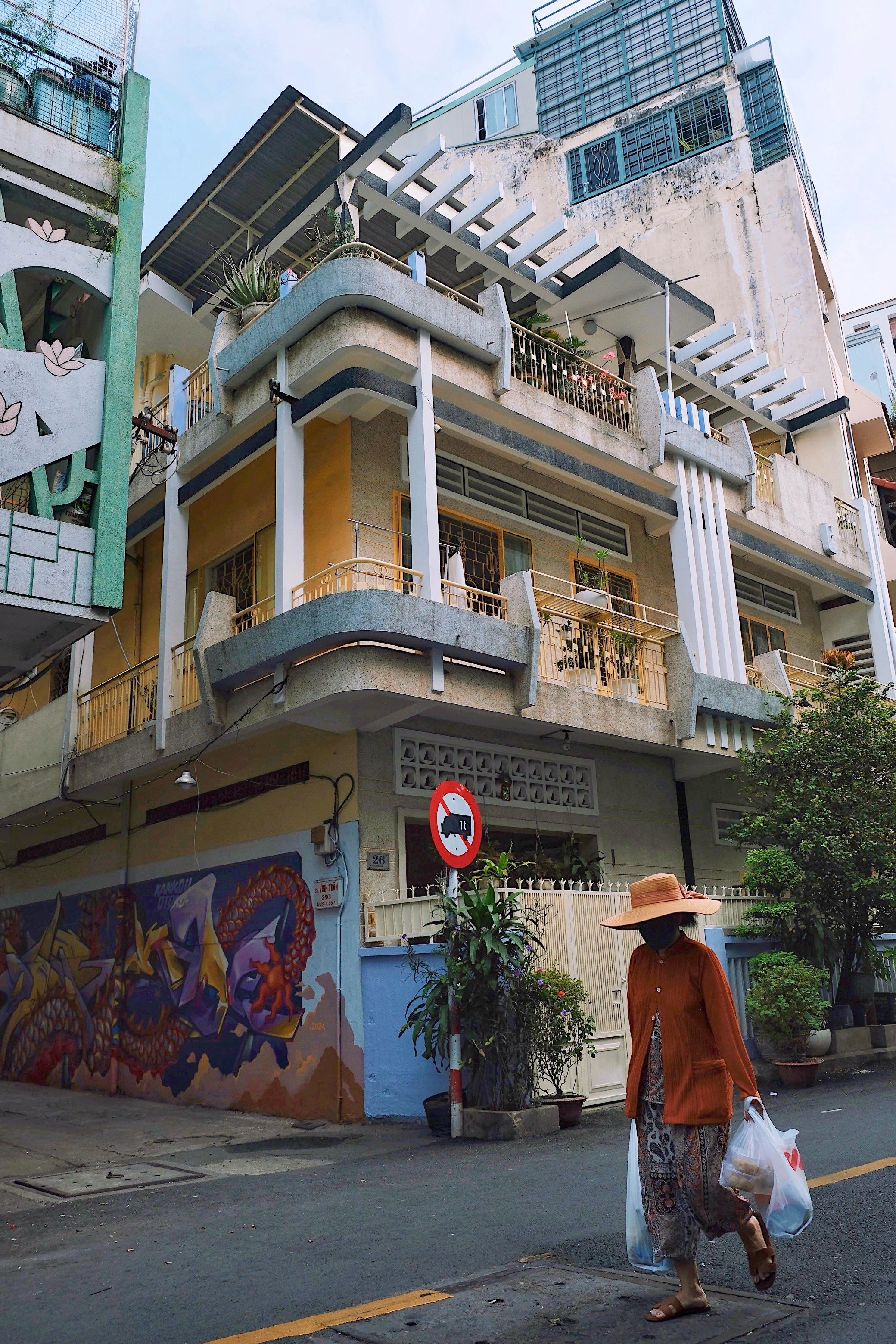 A street corner in Ho Chi Minh City, with a yellow modernist house, featuring lightweight concrete elements and functional tropical designs.