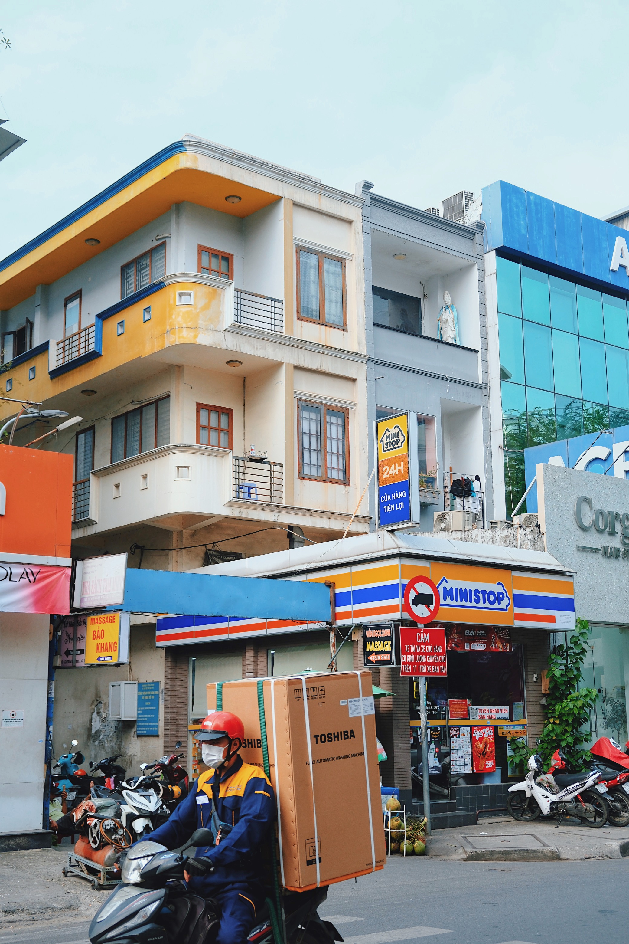 A delivery man in a blue and yellow suit riding past a modernist building in matching colors. Shot in Ho Chi Minh City, Vietnam.