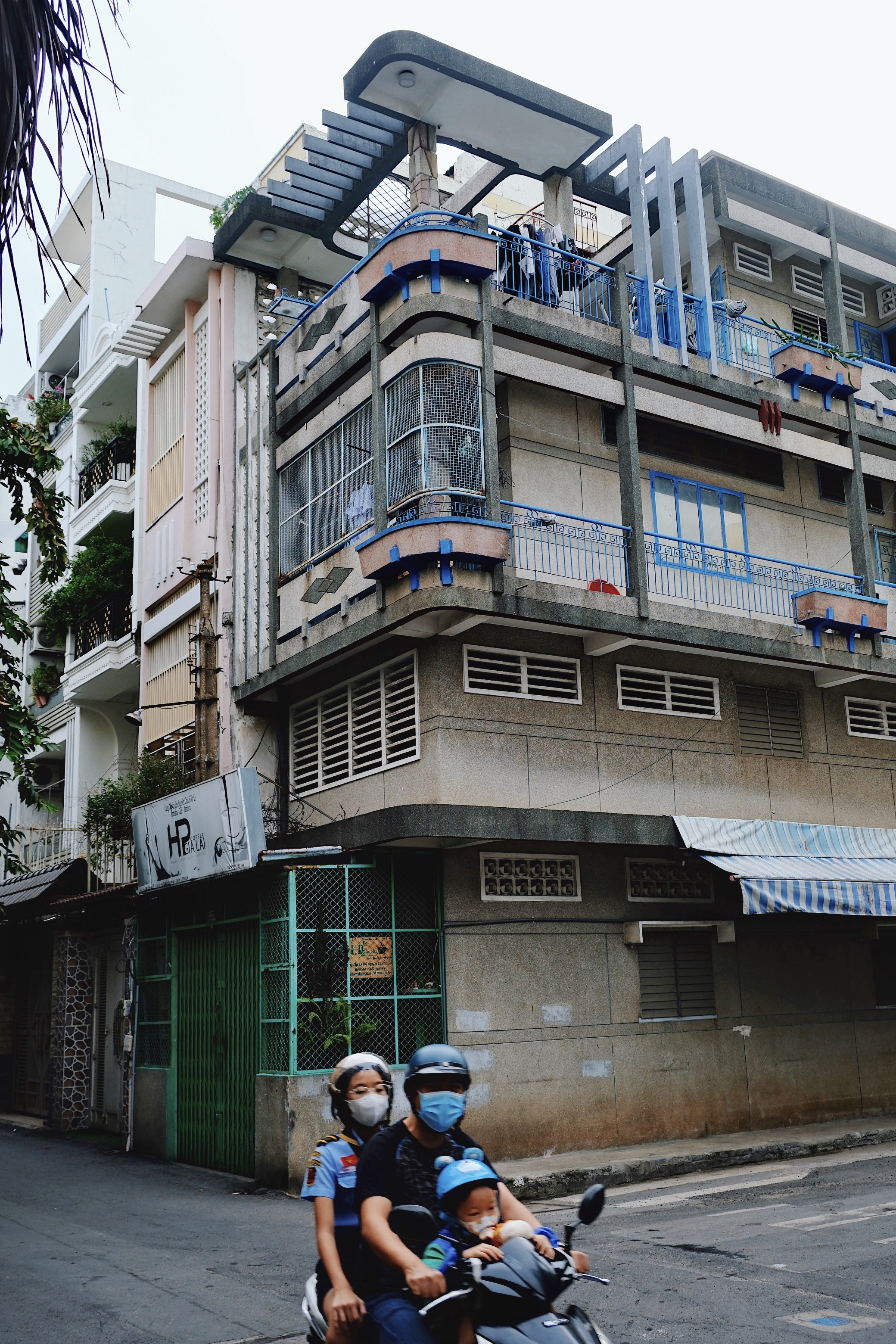 A family riding on a blue motorbike, perfectly matching the blue geometric concrete elements of the modernist building behind them.