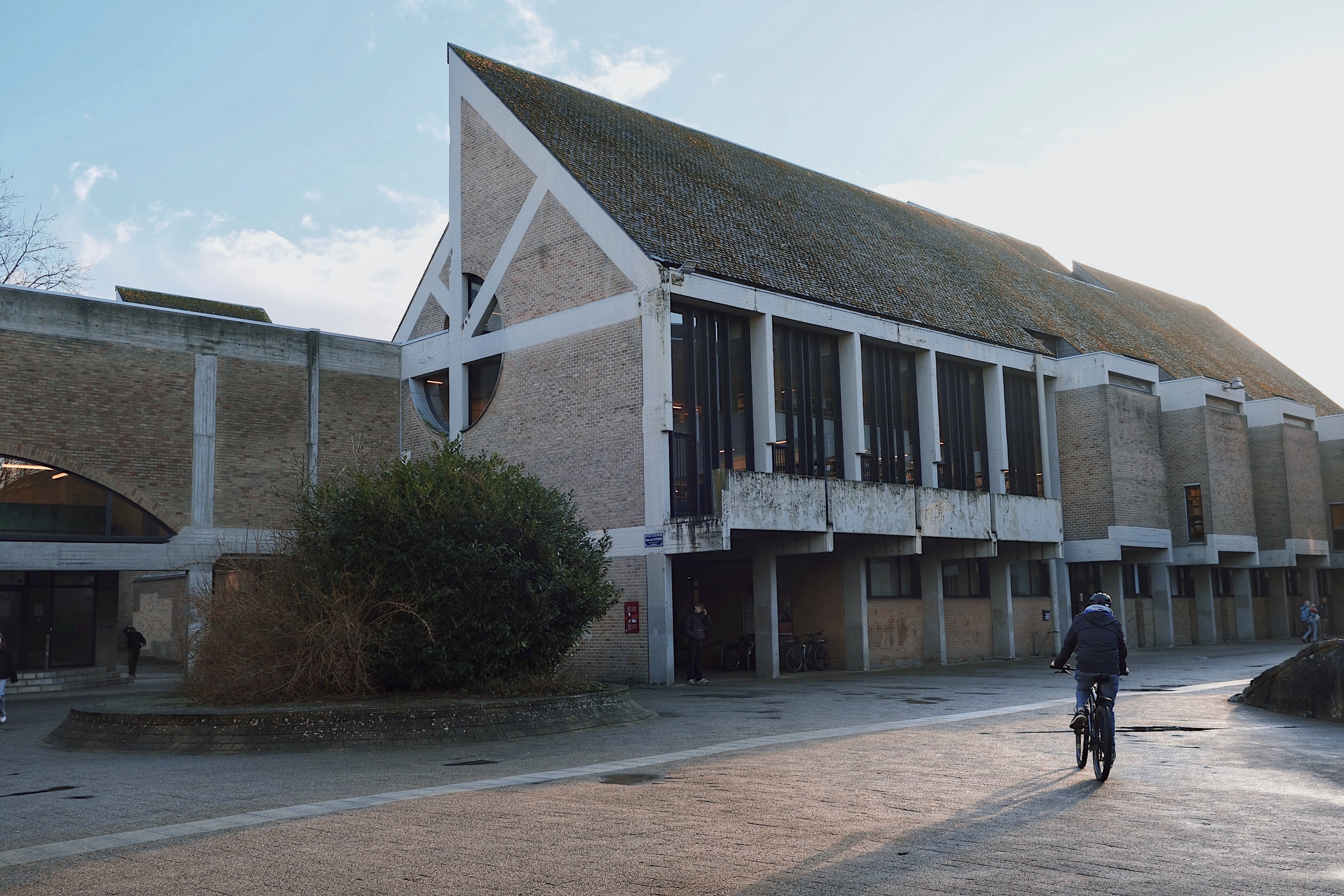 The economic and social sciences library in Louvain-la-Neuve, with a modernist sloped roof, exposed beams, and large vertical glass windows.
