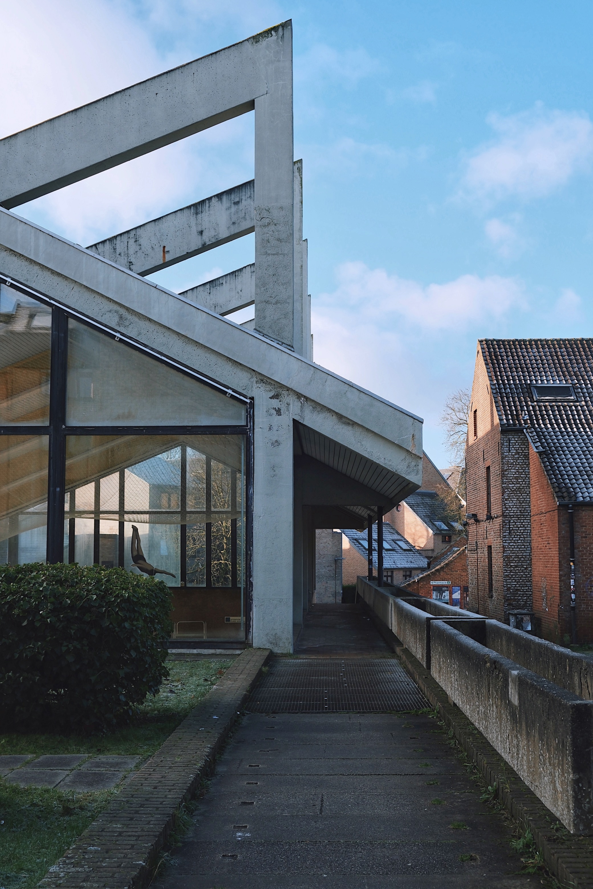 Blocry’s swimming pool in Louvain-la-Neuve, Belgium, features raw concrete beams and sloped glass walls, reflecting the functionalist aesthetic of 1970s Brutalism.