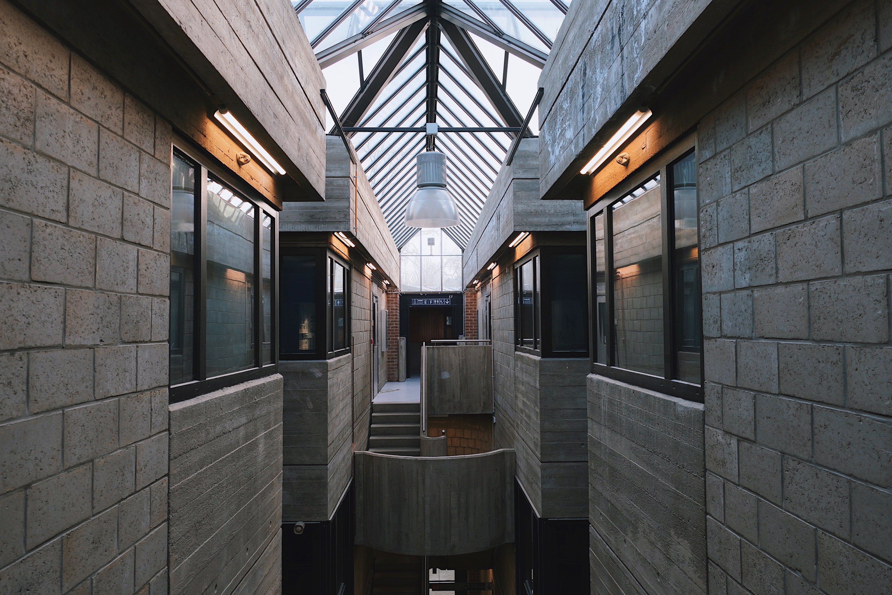  multi-level atrium in Louvain-la-Neuve’s Pierre Curie Building, where raw concrete meets brick textures, creating an industrial yet intimate academic space.