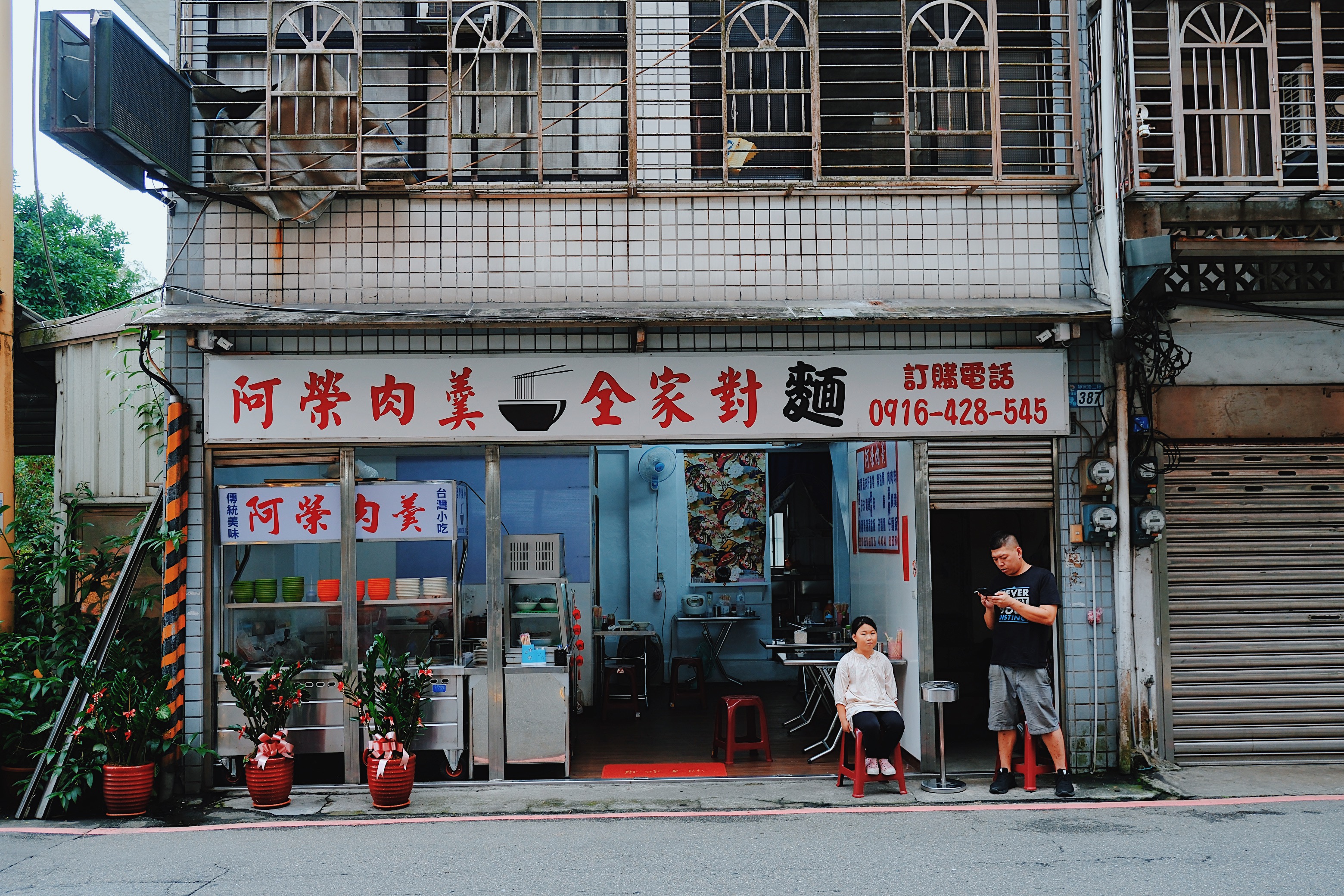  A family-owned noodle restaurant in Pingxi, Taiwan, with a retro storefront, hand-painted signage, and potted plants framing the entrance.