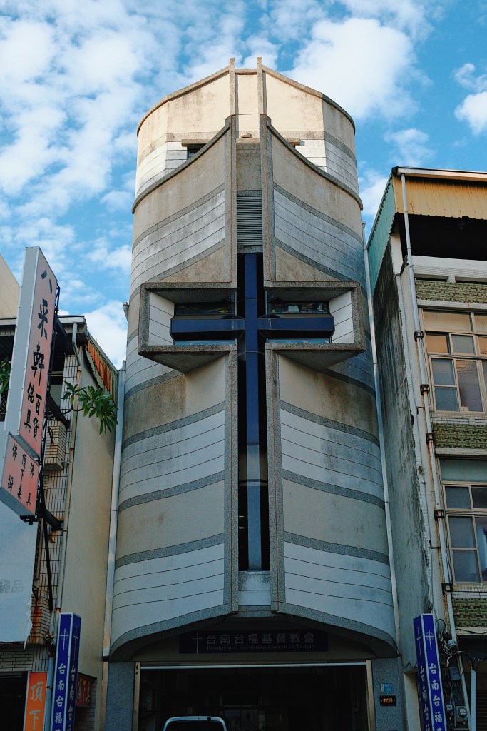 A striking Brutalist church in Tainan, Taiwan, with a bold geometric concrete design and a towering cross-shaped window at its center.
