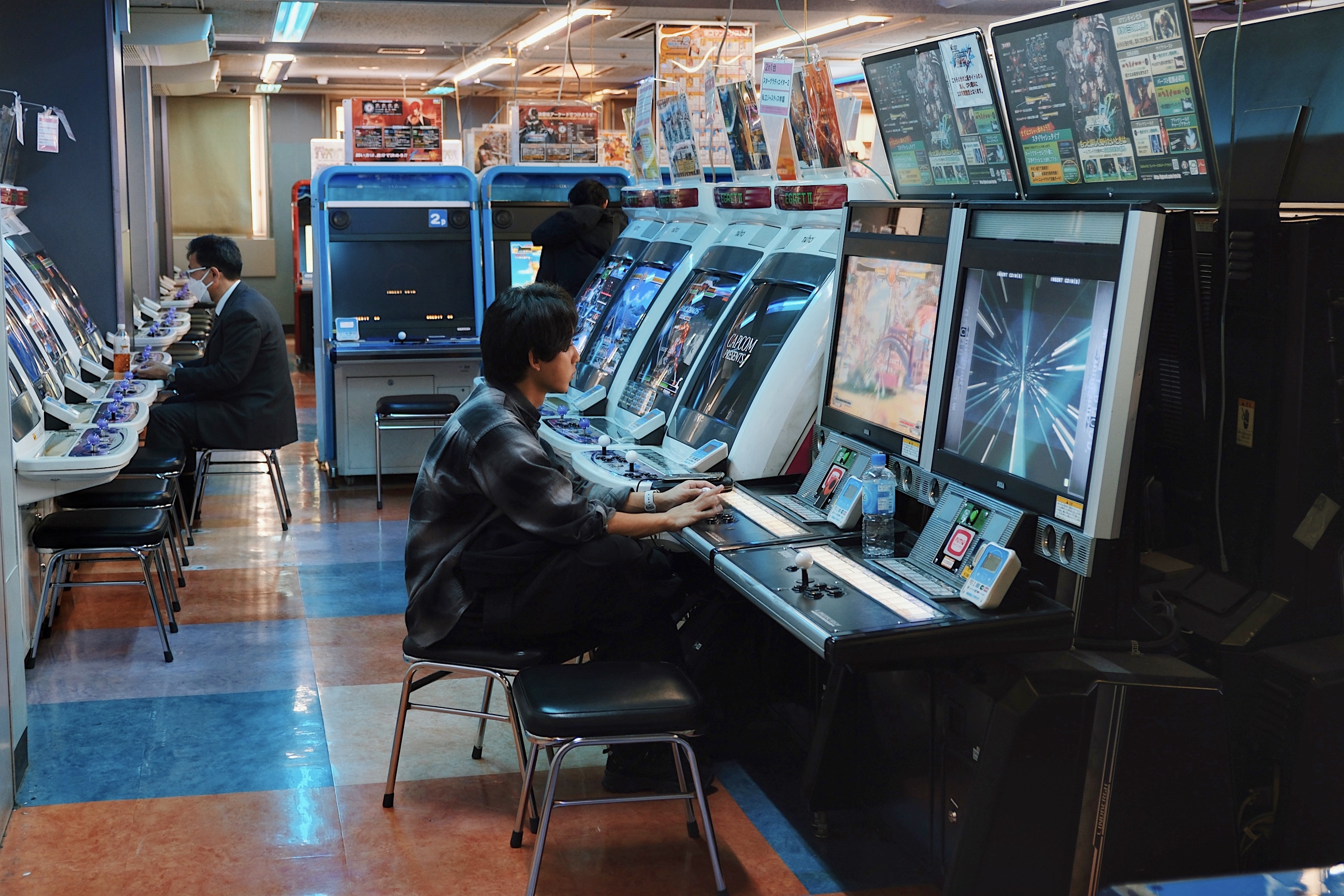 A cyberpunk-inspired gaming arcade in Akihabara, Tokyo, where players sit at retro gaming machines illuminated by the glow of LED screens.