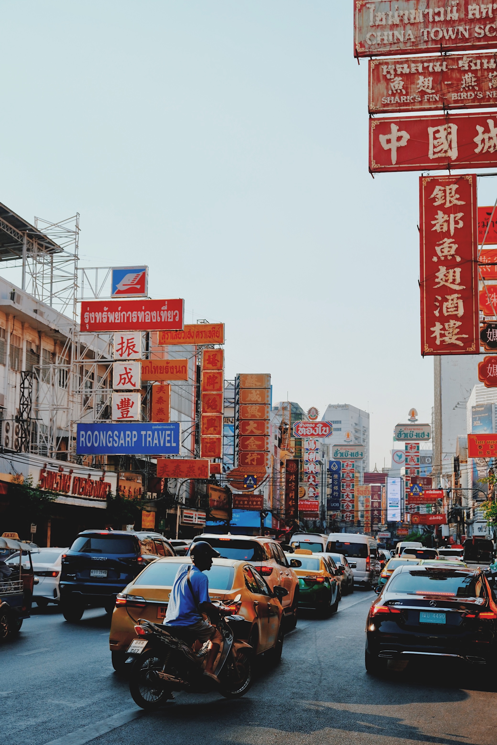 The lively streets of Bangkok’s Chinatown, filled with cars, motorbikes, and tuk-tuks, under a canopy of glowing Chinese neon signs.