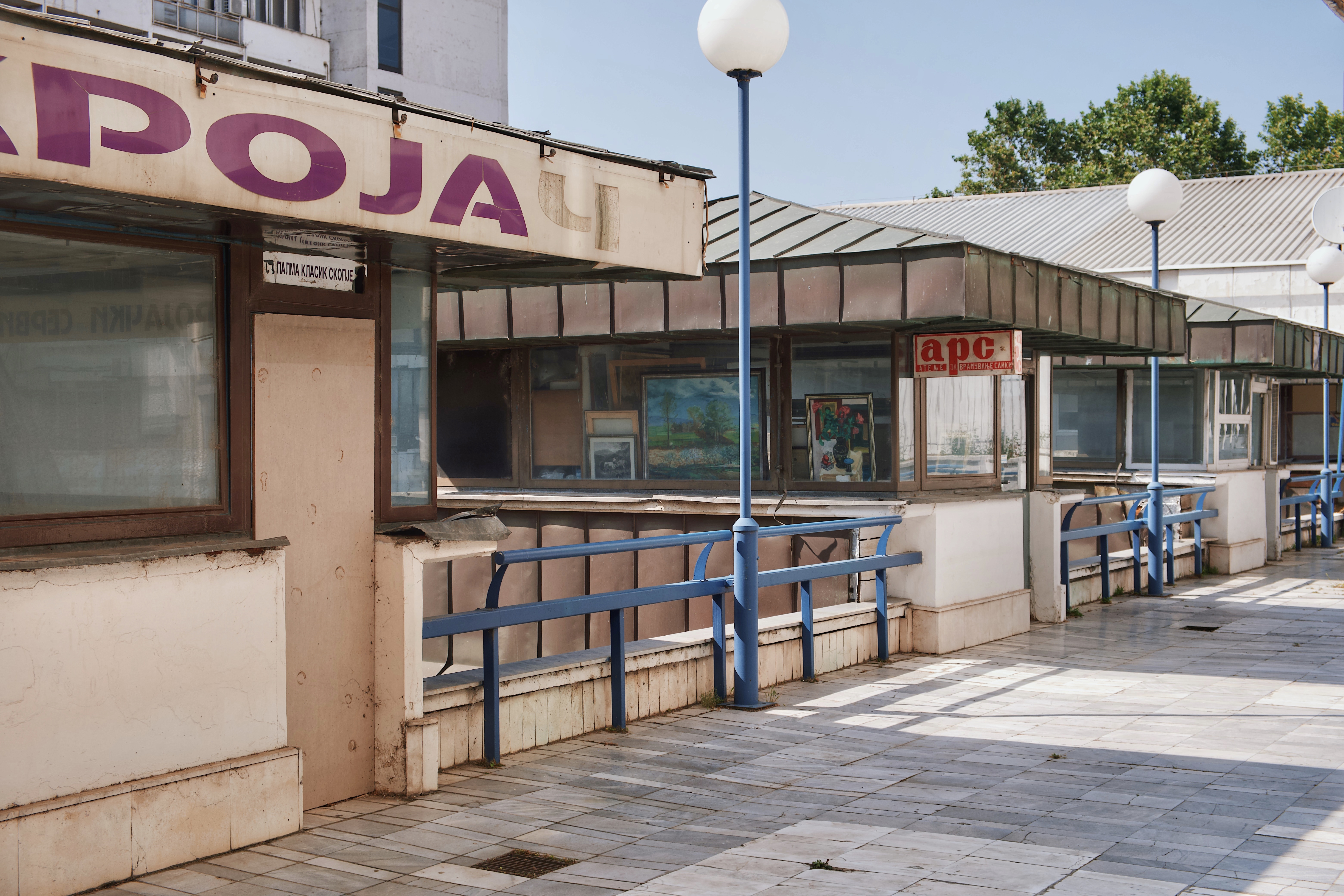 Exterior walkway of the City Trade Center in Skopje, North Macedonia, featuring vintage signage, tiled flooring, and glass-fronted brutalist-era kiosks