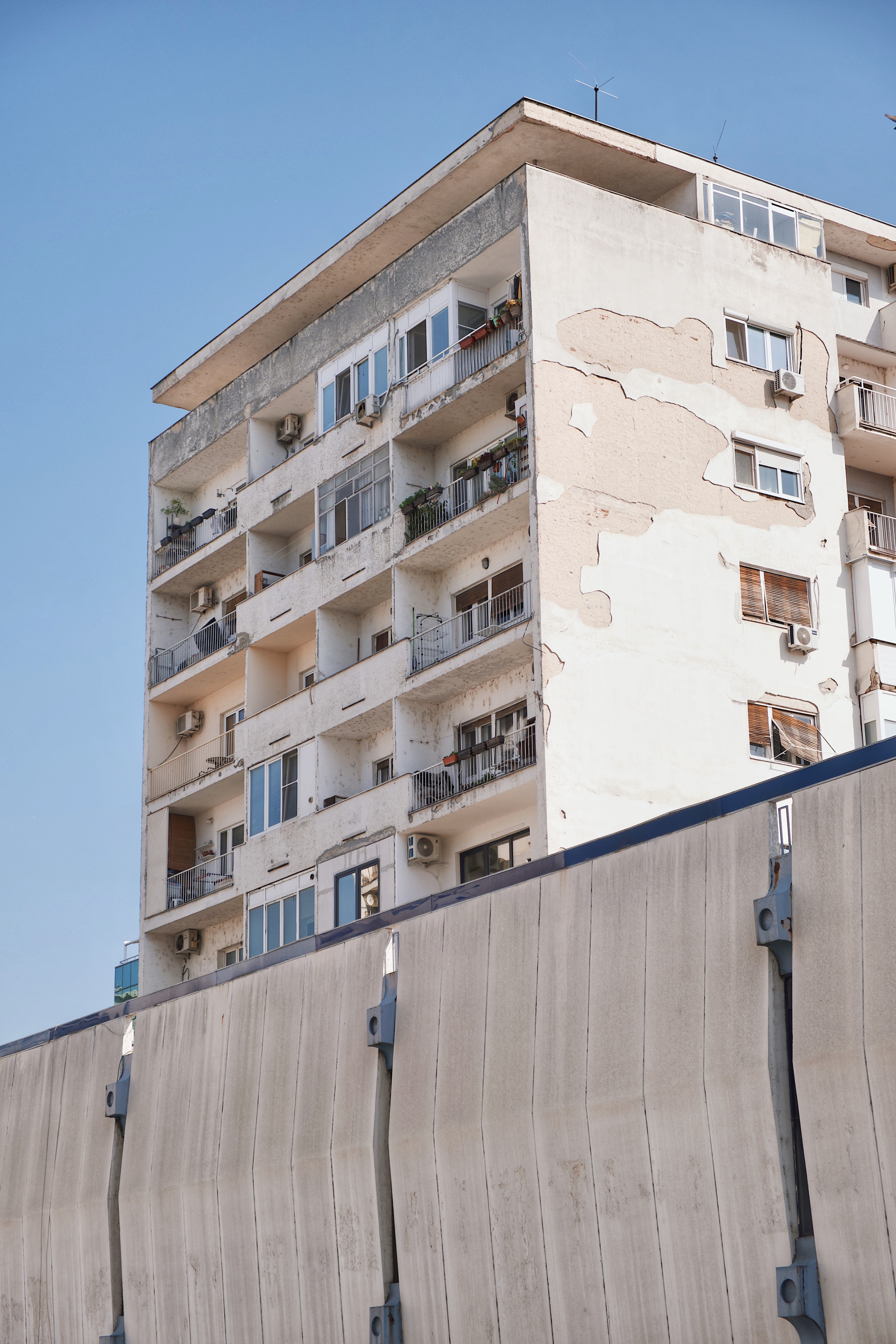 Residential building near City Trade Center in Skopje, showing weathered modernist architecture with peeling facade and exposed balconies behind a concrete barrier.