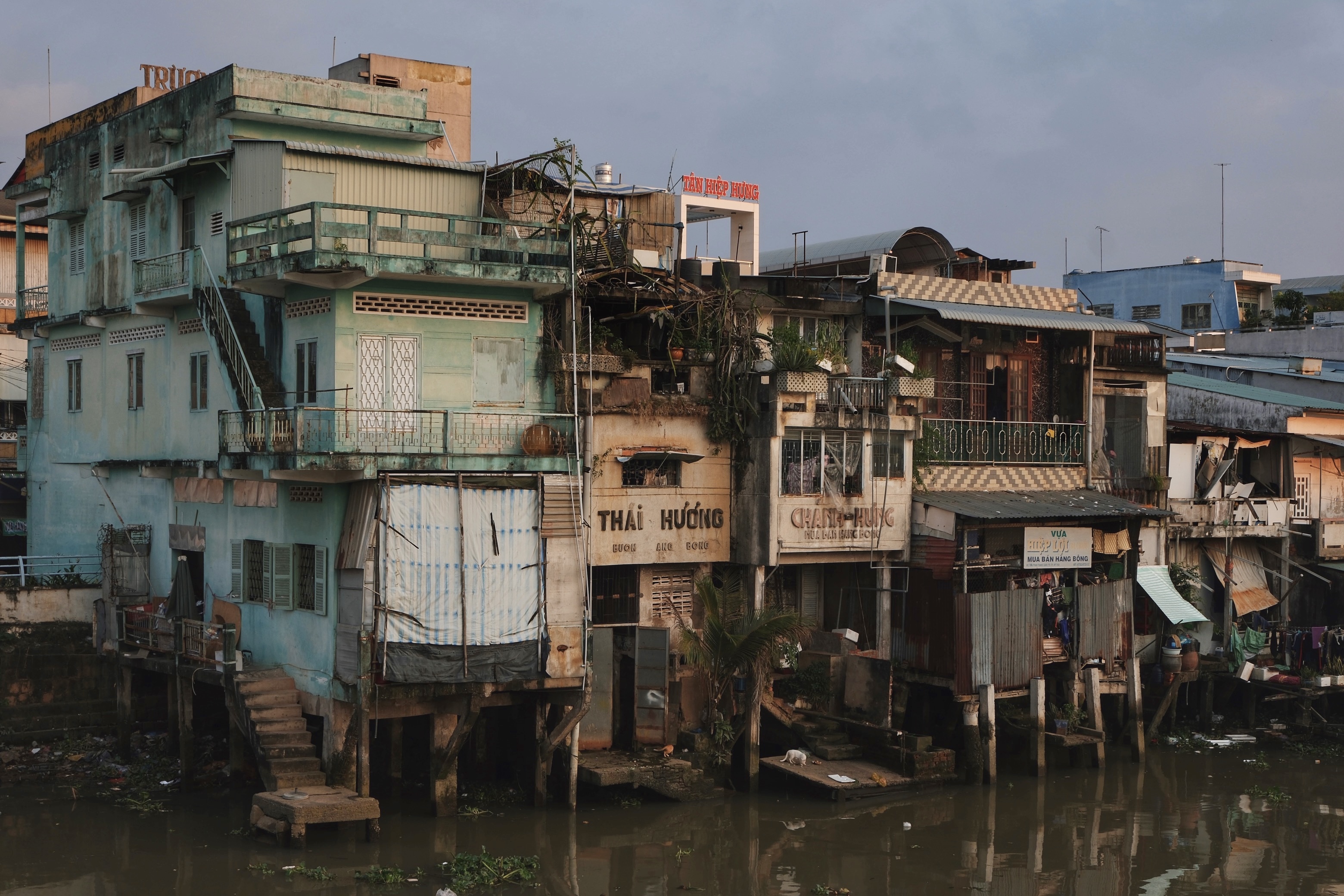 Architectural landscape of My Tho in the Mekong Delta, where traditional stilt houses and Southern Vietnamese modernist buildings line the river at dusk.